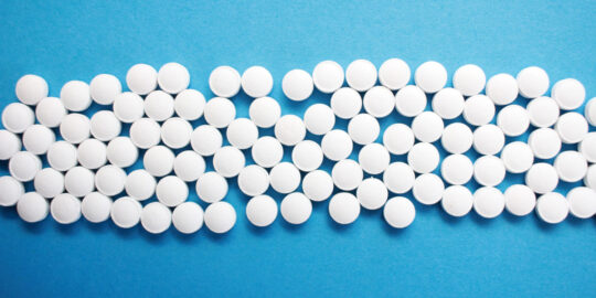 White circular pills on blue backdrop - NHS clinical and pharmaceutical waste services