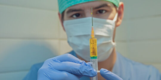 Doctor in scrubs and PPE with vaccine needle - Covid-19 PPE Waste